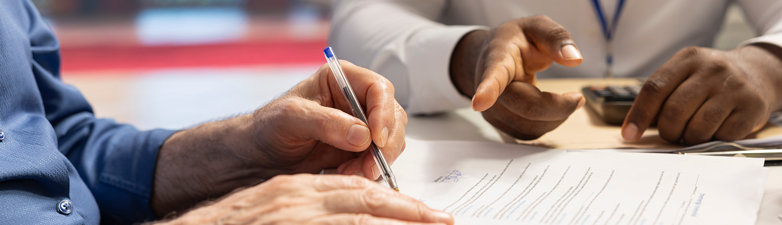 Close-up of a business meeting where one person signs a document while another points to a section